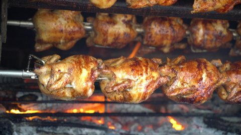 Grilled Rotisserie Chicken - Roasted chickens on spit grilled over wood fire on big bbq barbecue.