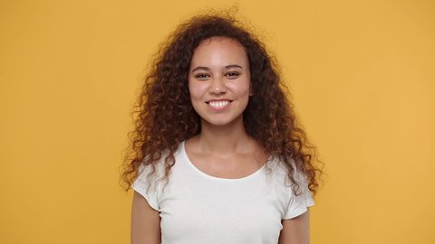 Young african american woman girl 20s years old in white t-shirt posing isolated on yellow background studio. People lifestyle concept. Dancing fooling around having fun expressive gesticulating hands