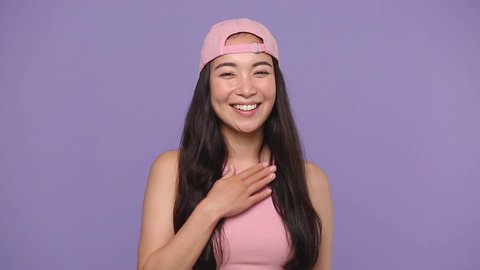 Young asian woman 20s years old in casual pink clothes cap posing isolated on pastel purple violet background studio. People lifestyle concept. Look camera smile send blow air kiss put hands on heart