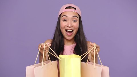Young asian girl 20s years old in casual pink clothes cap hold in hands look into package bags with purchases after shopping isolated on pastel purple violet background studio People lifestyle concept