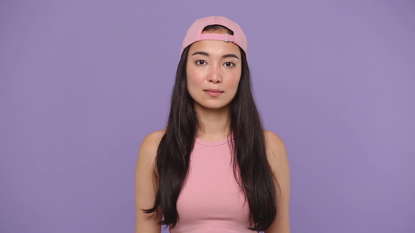 Fun confused shy shamed young asian woman girl 20s in pink clothes look camera bit lips spreading hands say oops i am sorry isolated on pastel purple violet background studio. People lifestyle concept | Shutterstock HD Video #1056010808