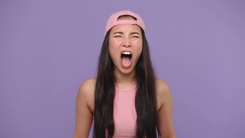 Angry mad sad swearing young asian woman girl 20s years old in casual pink clothes cap posing scream shout isolated on pastel purple violet background studio. People sincere emotions lifestyle concept