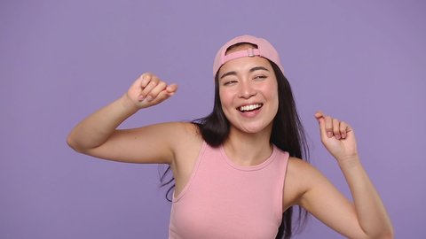 Young asian woman 20s in casual pink clothes cap posing isolated on pastel purple violet background studio. People lifestyle concept. Dancing fooling around having fun expressive gesticulating hands