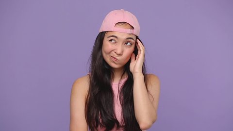 Young asian girl 20s in pink clothes cap posing Looks around thinks scratches at temple comes up with ideas raised finger up isolated on pastel purple violet background studio People lifestyle concept