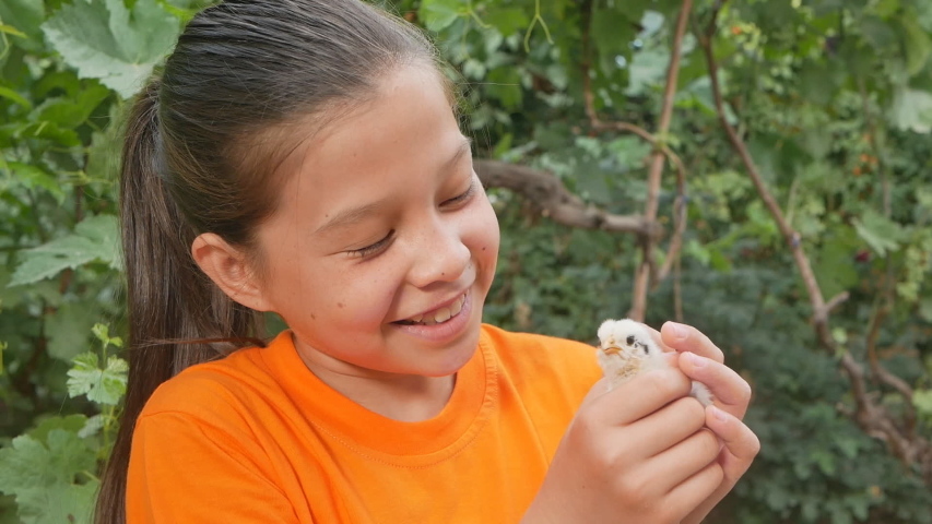 Cute happy teen girl is stroking a little chicken outdoors
