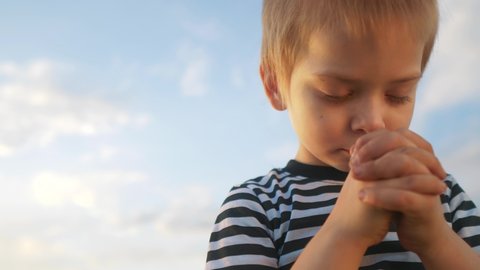 boy kid pray against a blue sky. child close-up concept faith religion and happy family. kid son jew crossed arms praying to god. kid catholic pray worship and gratitude and a happy childhood
