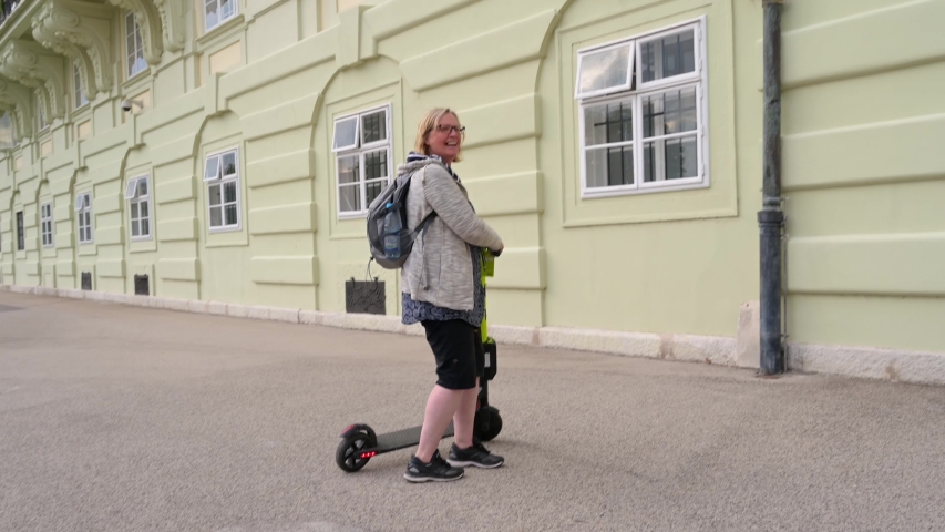 VIENNA - JULY 11, 2019: A happy woman rides a rental electric scooter | Shutterstock HD Video #1056012809