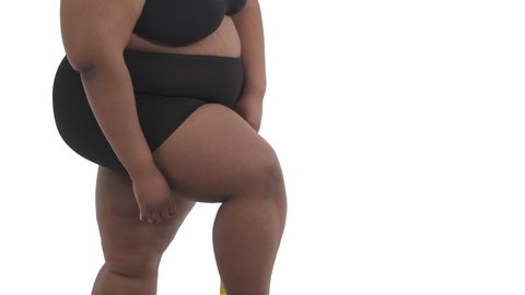 Close-up of unrecognizable african american obese woman's body in underwear measuring her thigh isolated on white background