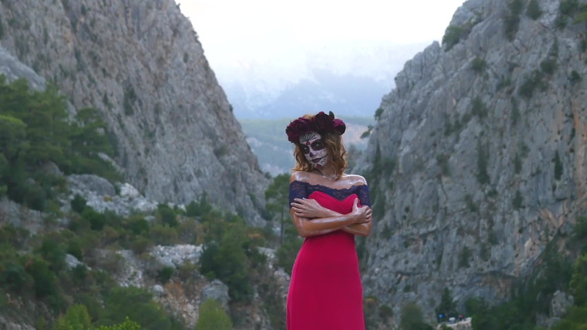 Santa Muerte makeup woman in pink dress on Halloween eve outdoors mountain background