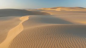 Calming abstract wavy texture on the wild desert surface. 4K drone view over the scenic massive golden dunes and blue sky above. Beautiful aerial video of nature landscape at sunrise, California, USA