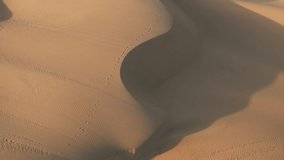 Wild nature landscape. A lonely traveler in fashion red fluttering dress is walking by golden sand dunes. 4K aerial slow motion video of a beautiful girl in the desert at sunset, California