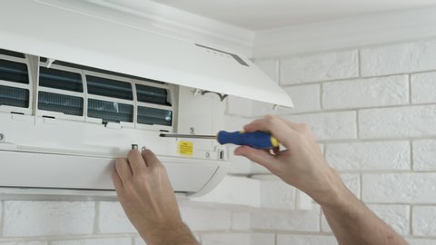 Air conditioning repair. A man with a screwdriver at the air conditioner. Maintenance of domestic air conditioners.