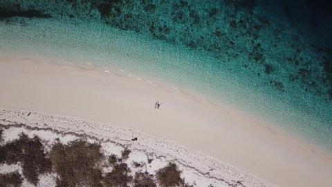 A drone shot of a couple lying at the shore of white sand beach on a small island near Maumere, Indonesia. Happy and careless moments. Waves gently washing the shore. Romance and love while travelling