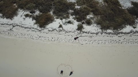 A drone shot of a couple drawing a heart on the white sand beach on a small island near Maumere, Indonesia. Happy and careless moments. Waves gently washing the shore. Romance and love. Happiness
