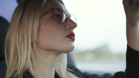 Glamorous lady in glasses applying the red pomade at mirror in the car. 4K