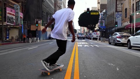 LOS ANGELES, CA, USA - JUNE 5, 2020: Black cool skateboarder jumping trick on street in Los Angeles. American hipster. Urban healthy active lifestyle, adventure, sport & summer in LA. Slow motion 4k. 