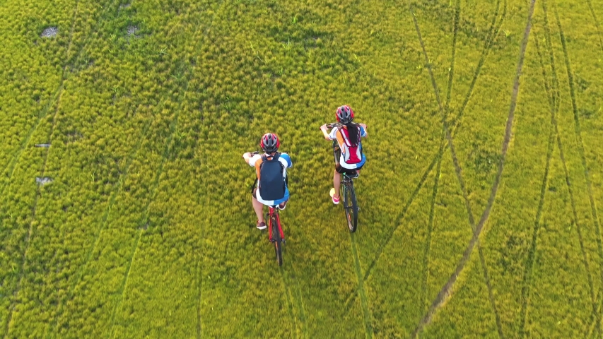 Footage B Roll 4k. Aerial view Drone tracking young People riding a bikes on the meadow, aerial view. Love Couple cycling on green lawn together, aerial drone view. Healthy lifestyle concept. | Shutterstock HD Video #1056029945