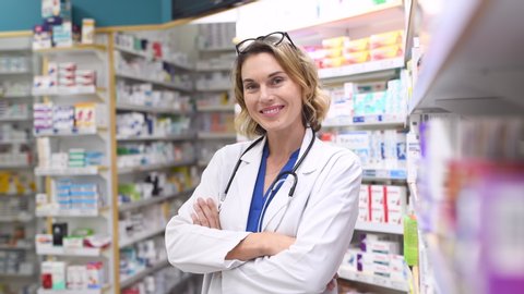 Portrait of mature woman pharmacist at pharmacy wearing labcoat with stethoscope. Happy smiling doctor standing in pharmacy drugstore. Friendly pharmacist owner standing in shop and looking at camera.