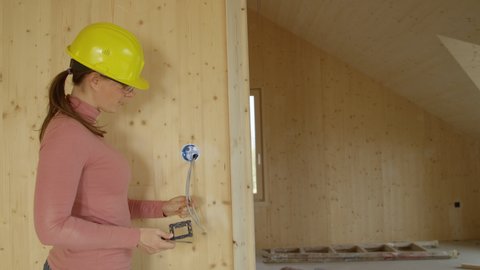SLOW MOTION, COPY SPACE, CLOSE UP: Young female electrician screws a small frame in place of a light switch on a wooden wall. Woman working at construction site installs an outlet onto wooden wall