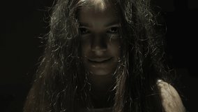 Portrait of a scary young girl in a dark room with flickering light, the girl raises her hands and takes off the chain. Useful for horror, Halloween, scary, nightmare videos.