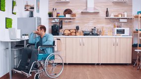 Happy disabled man in wheelchair using laptop in kitchen. Man talking on video conference. Corporate man with paralysis handicap disability handicapped difficulties working after accident having