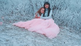 Beautiful happy young woman mom tenderly hugs little girl daughter, sit relax in winter forest. Smiling joyful faces. Two people concept love. Same clothes, warm blue sweater, long luxury skirt dress