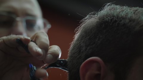 Hairdresser at barbershop doing short male haircut using scissors. Close up shot of barber working to cut hair of customer.