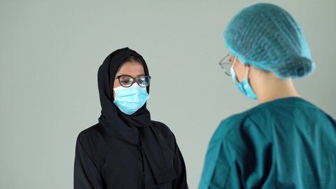 Nurse in a medical mask, glasses and gloves measures the Arab woman patient's temperature with a non-contact infrared thermometer.