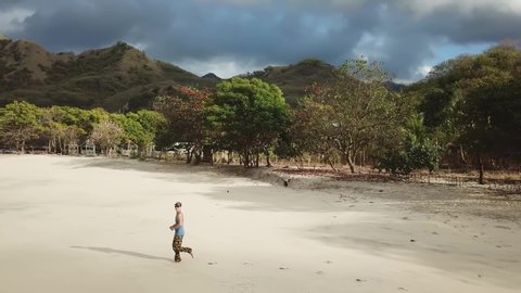 A man running towards a woman in idyllic Koka Beach. Hidden gem of Flores, Indonesia. Couple is enjoying their romantic escape. Waves gently washing the shore. There are hills in the back. Fun and joy