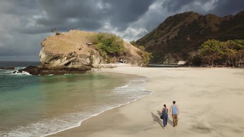 A man running towards a woman in idyllic Koka Beach. Hidden gem of Flores, Indonesia. Couple is enjoying their romantic escape. Waves gently washing the shore. There are hills in the back. Fun and joy