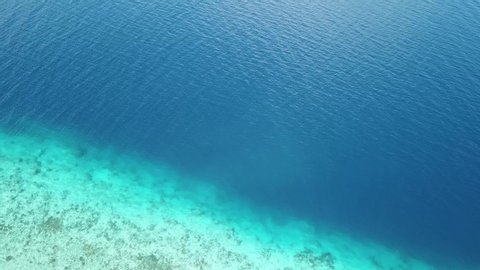 A drone shot a crystal clear sea water near the coast of Maumere, Flores, Indonesia. The turquoise water lets us see the coral reef. Deeper water is dark blue. Serenity and calmness. Hidden gem
