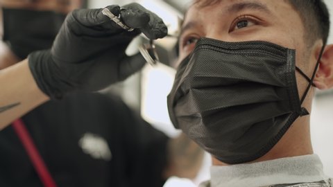 Asian young Male close up face get a Hair Cut scissors trimming hair at the Barbershop wear black protective mask. job opportunity, service job start up business, Pandemic Covid-19 re-open business - Βίντεο στοκ