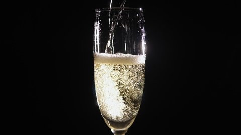 Close-up of the bartender pouring champagne into a glass on a black background, the glass has a lot of foam and bubbles. Artificial lighting. Slow motion.