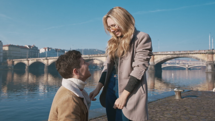 Happy woman taking a proposal about wedding and kissing her future husband. Handsome young man giving an engagement ring to her girlfriend. Couple dating on the bridge. Concept of love and marriage. Royalty-Free Stock Footage #1056045440