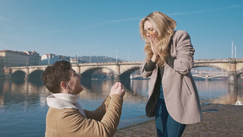 Happy woman taking a proposal about wedding and kissing her future husband. Handsome young man giving an engagement ring to her girlfriend. Couple dating on the bridge. Concept of love and marriage. Royalty-Free Stock Footage #1056045440