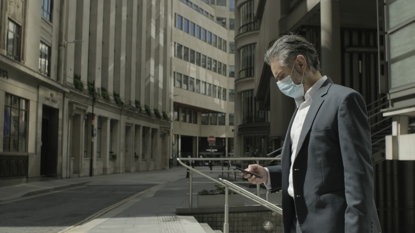 Corporate business man commuting to work wearing face mask and using smart phone in the city of London during Covid-19 Pandemic Royalty-Free Stock Footage #1056046832