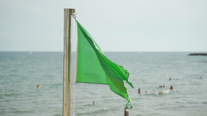 Slow motion Green safety flag flying in a stiff breeze at the beach: swimming allowed. . Shot from original 120 fps Royalty-Free Stock Footage #1056046937