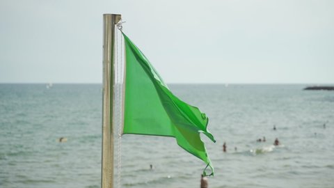 Slow motion Green safety flag flying in a stiff breeze at the beach: swimming allowed. . Shot from original 120 fps