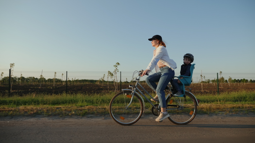 Happy mother with her smiling little son are riding a bike on the road at sunset, slow-motion Royalty-Free Stock Footage #1056048248