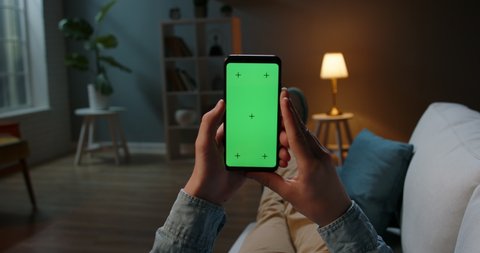 Close up shot of guy lying on couch at night, holding a smartphone with chroma key mock up green screen - technology, connections, communications concept 4k video template