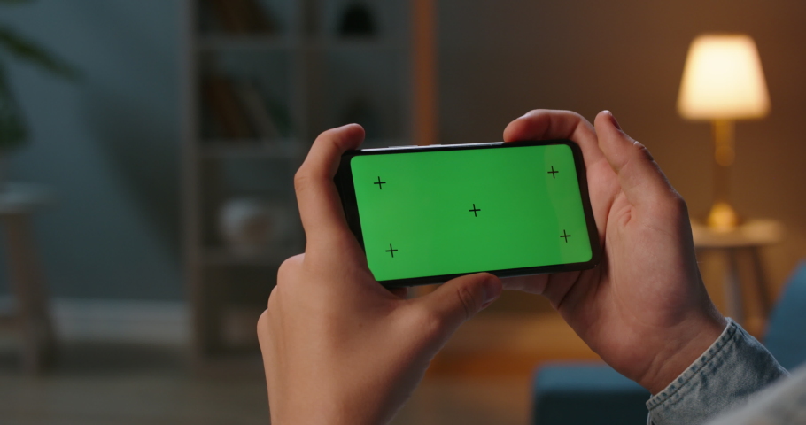 Close up shot of guy using his horizontal smart phone with mock up green screen at night, using various gestures while watching a video 4k video template Royalty-Free Stock Footage #1056049013