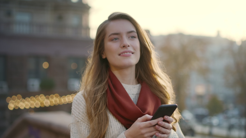 Portrait of happy hipster woman typing by mobile phone outdoors. Closeup cheerful girl walking with smartphone in urban background. Smiling lady holding cellphone in hands outside. | Shutterstock HD Video #1056052220