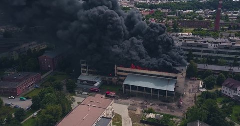 Aerial Footage of Firefigters Trying to Extinguish a Large City Building Ablaze. Clouds of Black Thick Smoke and Bright Flames Rising into the Air from the Strongly Burning Industrial Building or