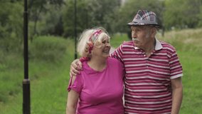 Senior caucasian couple walking and talking in summer park embracing. Happy family enjoying time together after retirement. Elderly man walks with woman and hugs her. Husband, wife. Grandpa, grandma
