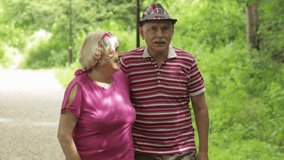Senior caucasian couple walking and kissing in park. Embracing. Active modern life after retirement. Happy family enjoying time together. Elderly man walks with woman. Husband, wife. Grandpa, grandma