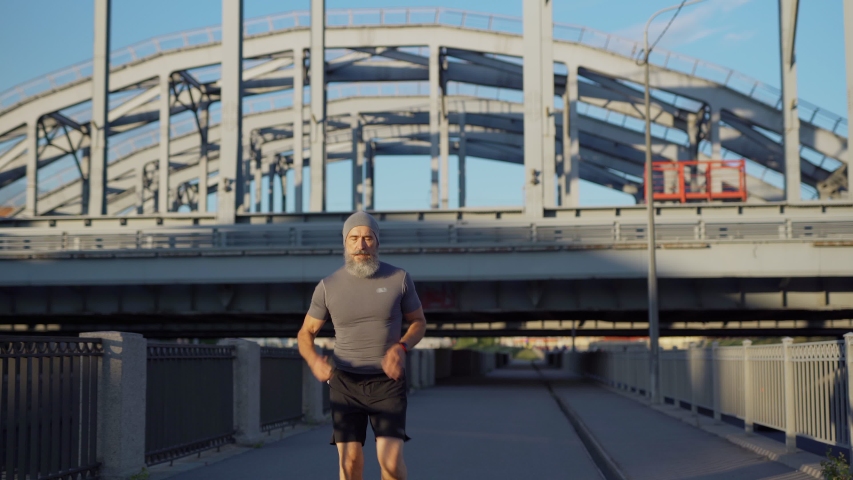 Medium shot of senior man with grey beard finishing running workout, catching breath and checking pulse or race time on smartwatch and in mobile app on smartphone Royalty-Free Stock Footage #1056057743