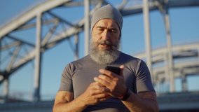 Medium shot of senior man with grey beard finishing running workout, catching breath and checking pulse or race time on smartwatch and in mobile app on smartphone - Powered by Shutterstock - Get 15% off with code: PIKWIZARD15
