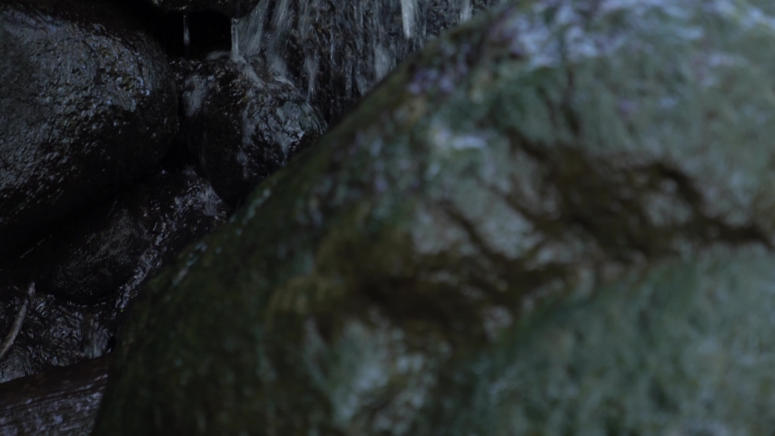Close up vertical pan of white water flowing over the rocky surface of a man made waterfall cascade with wet slippery boulder rocks covered in dark green algae in the foreground.