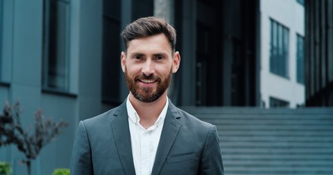 Portrait of Amazing Caucasian Businessman is smiling sincerely to the Camera. Handsome Man in Suit is standing near Business Office. Concept of: Business, Successful People, Smart People, busy Life.