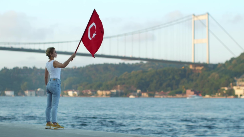 The woman is holding the flag of the Republic of Turkey, shaking the Bosporus.